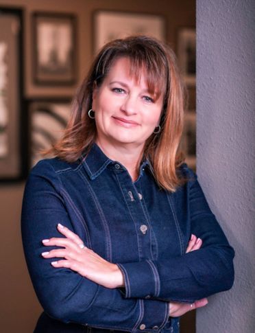 A woman in a blue shirt is standing with her arms crossed.