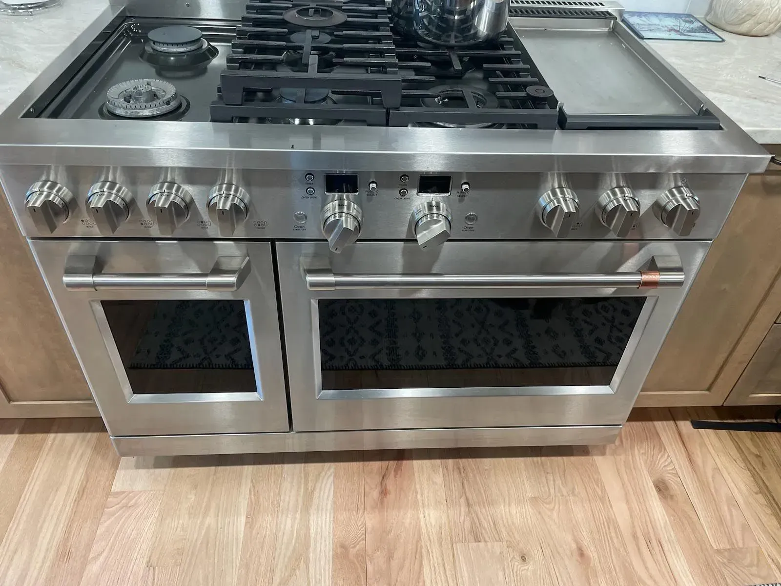 A stainless steel stove top oven is sitting on a wooden floor in a kitchen.