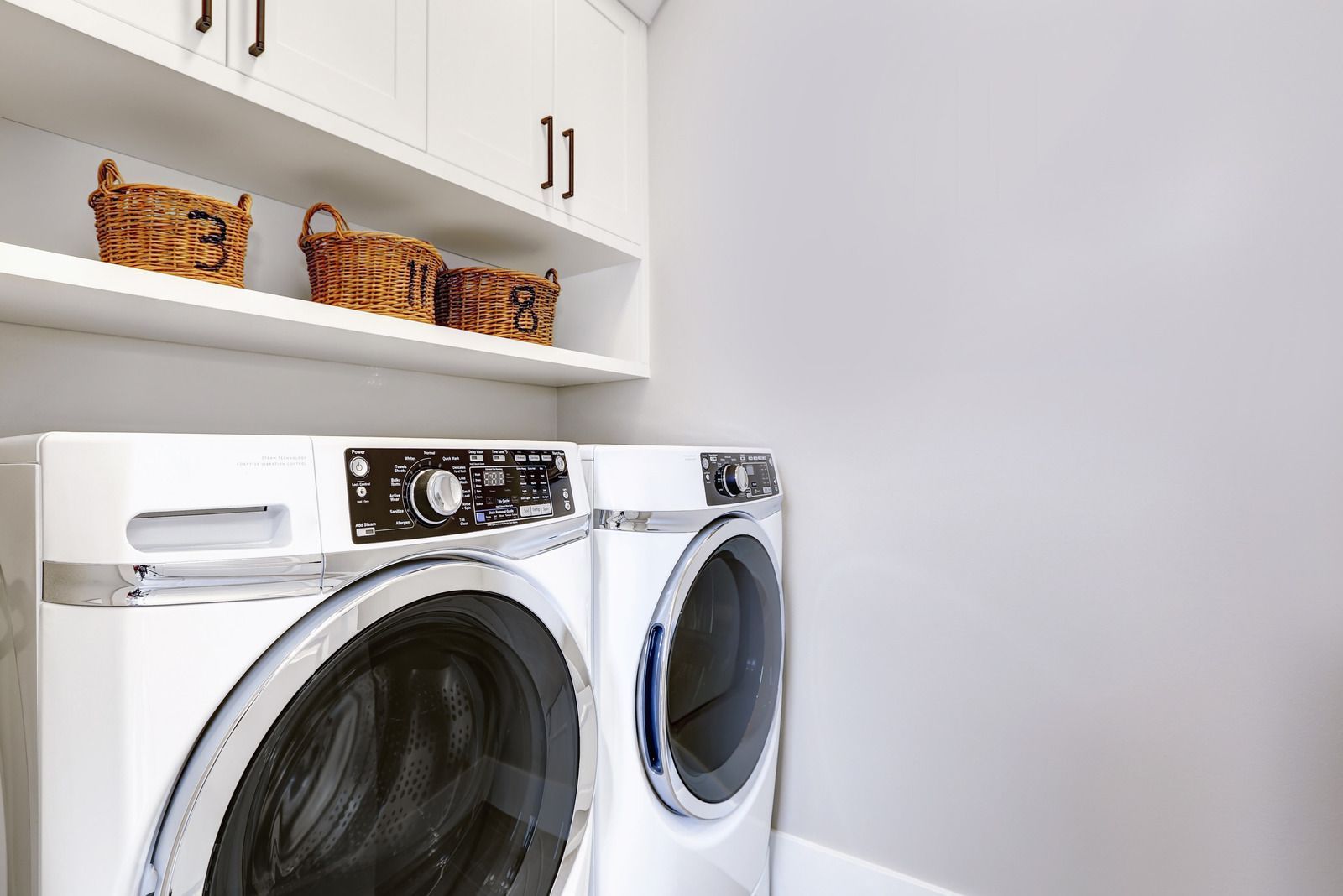 A laundry room with a washer and dryer and baskets on the shelves.