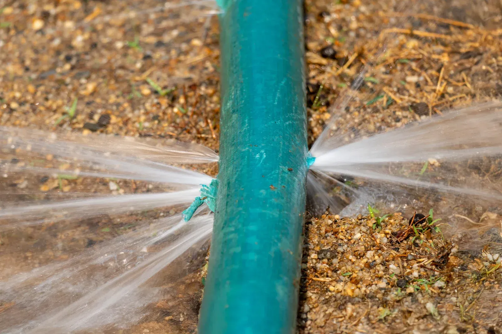 Damaged blue pipe with water spraying out.