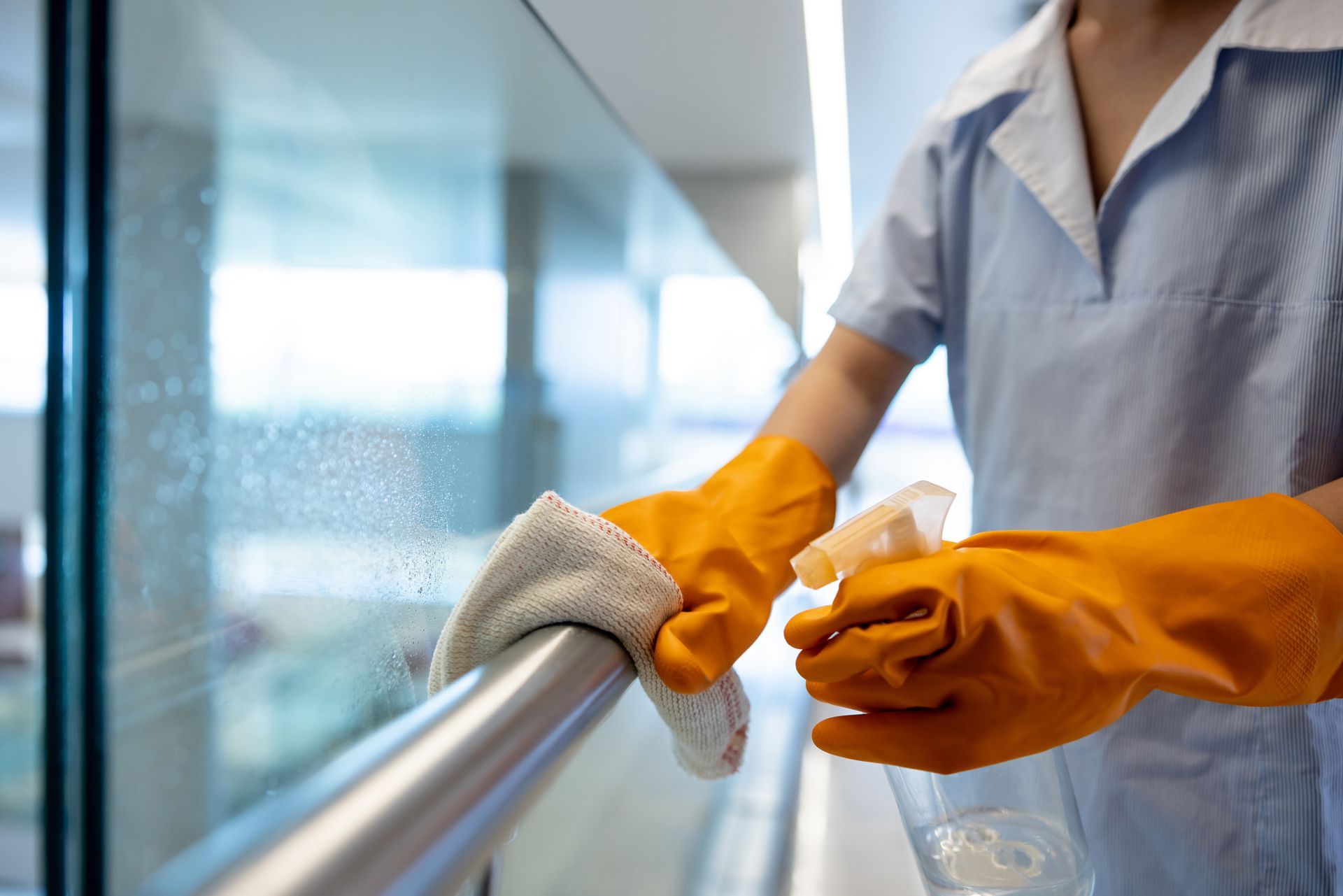 A woman wearing orange gloves is cleaning a railing with a cloth.