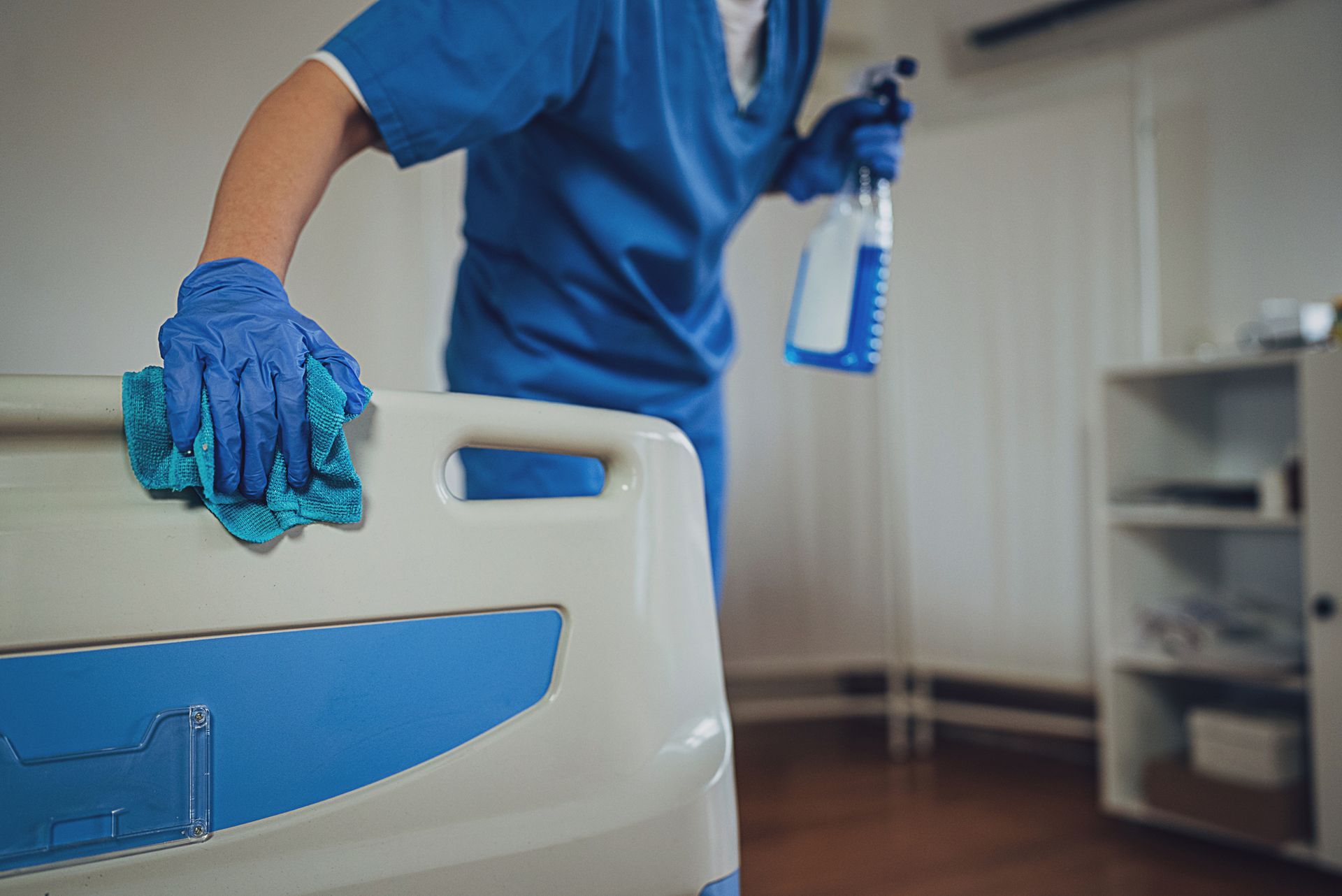 A nurse is cleaning a hospital bed with a cloth and spray bottle.