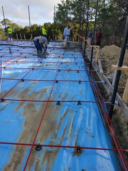 Construction site: workers laying rebar grid on blue tarp covering a concrete slab.
