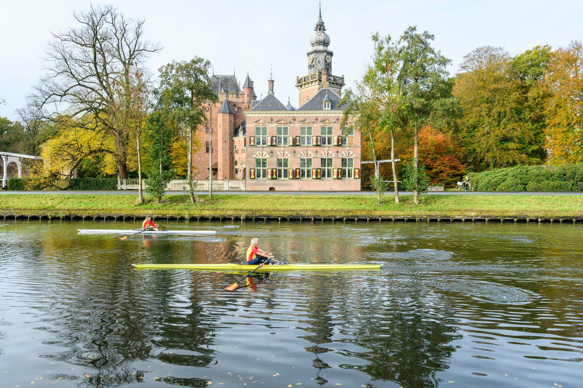 Een man peddelt in een kajak op een rivier voor een kasteel.