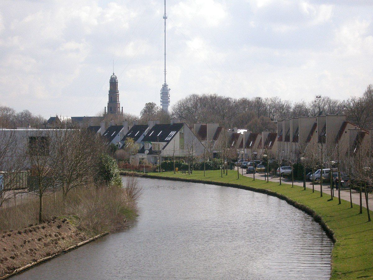 Een rivier stroomt door een woonwijk met een toren op de achtergrond