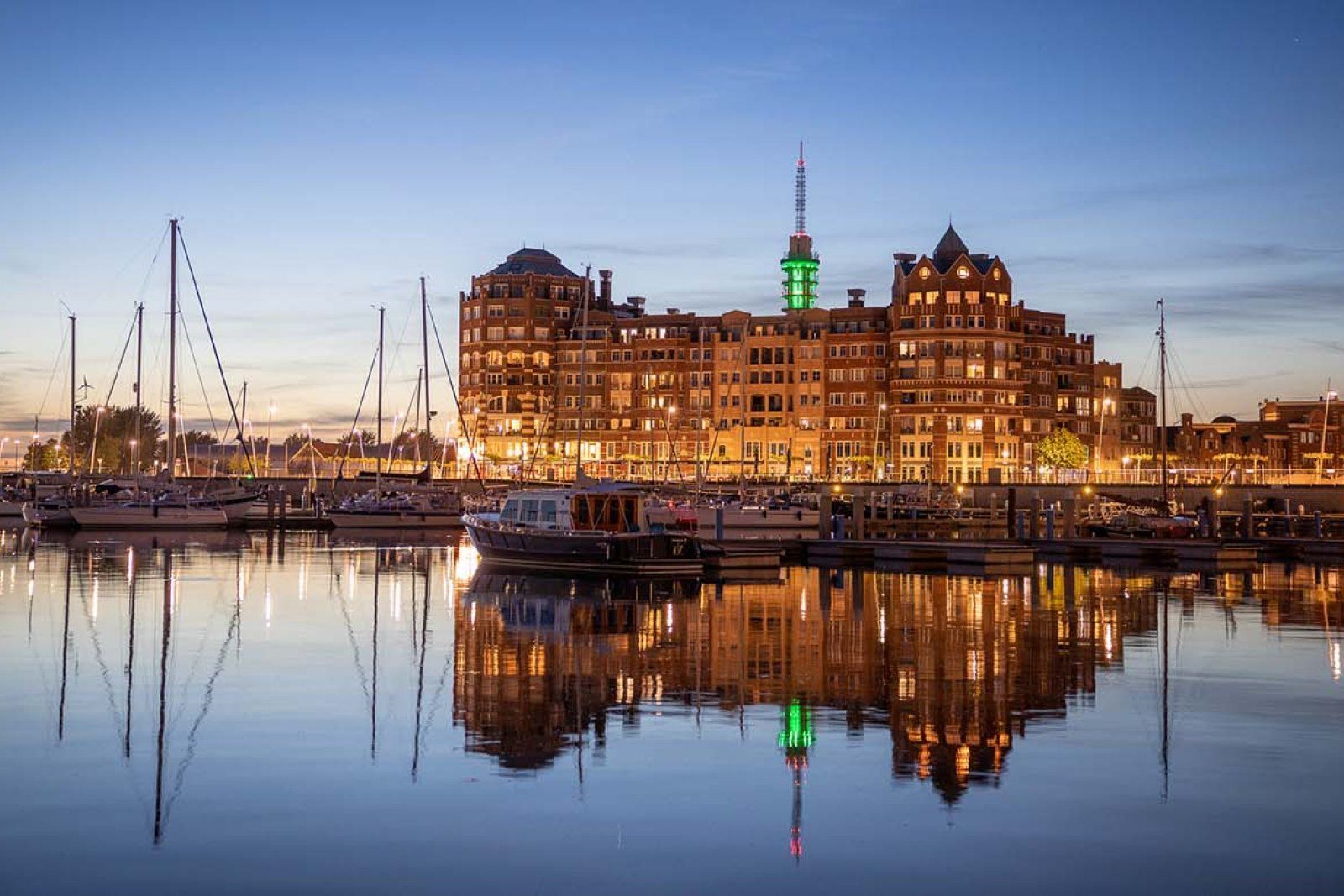Een groot gebouw weerspiegelt zich 's nachts in het water van een haven.