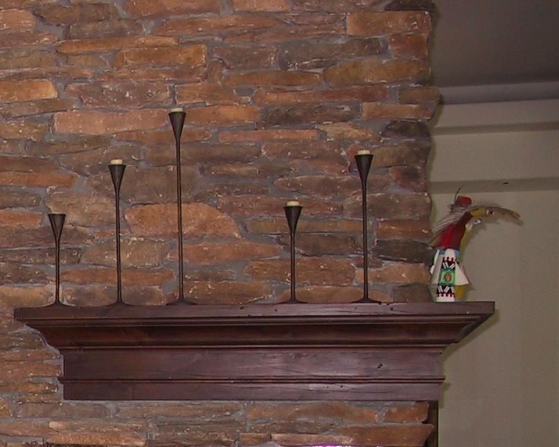 A wooden mantle with candles on it in front of a brick wall