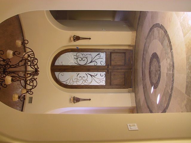 Beige arched hallway with wooden double doors, decorative glass, and a circular floor inlay.