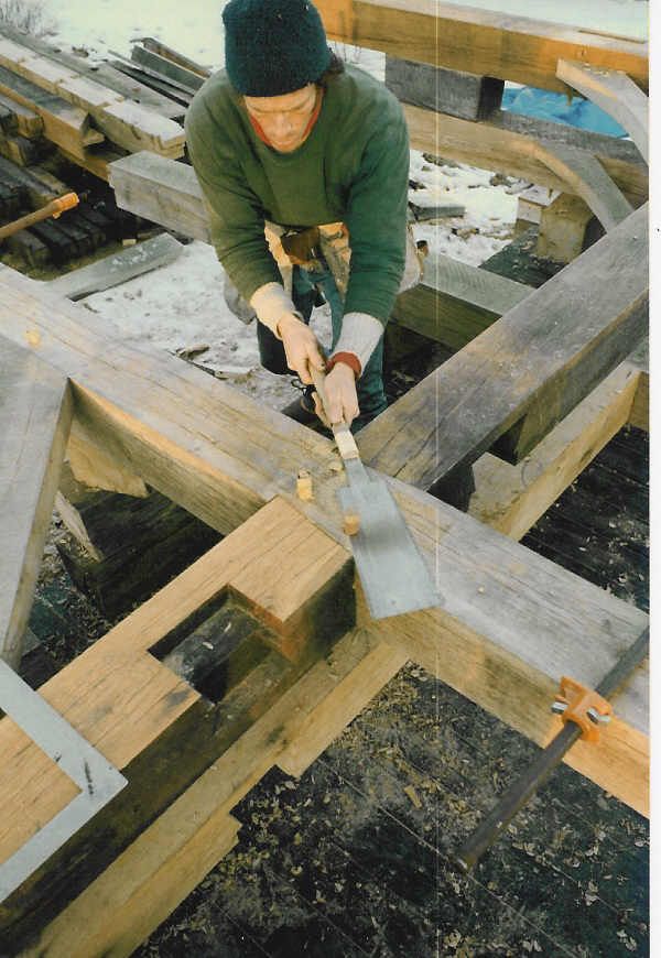 A man in a green sweater is working on a wooden structure