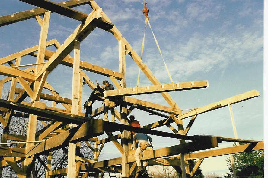 A construction worker is standing in front of a wooden house under construction.