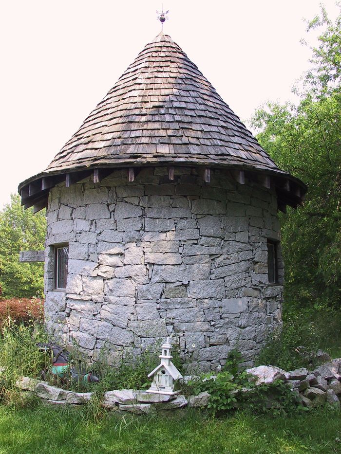 A stone building with a wooden roof is surrounded by trees and grass.