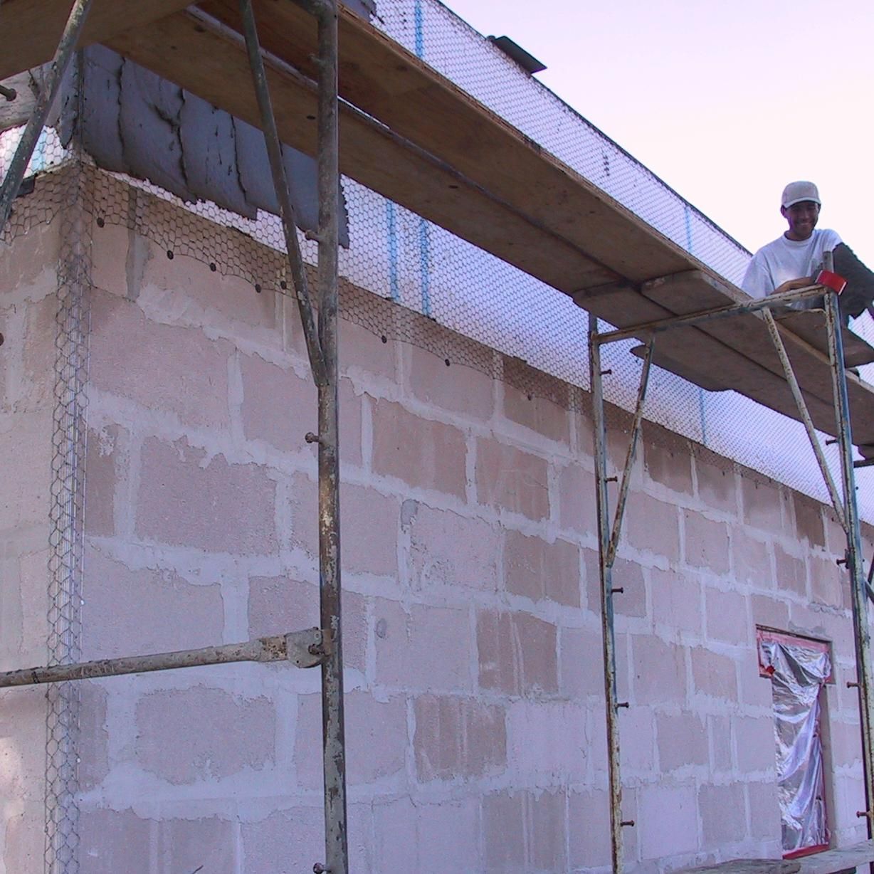A man is standing on a wooden scaffolding over a brick wall