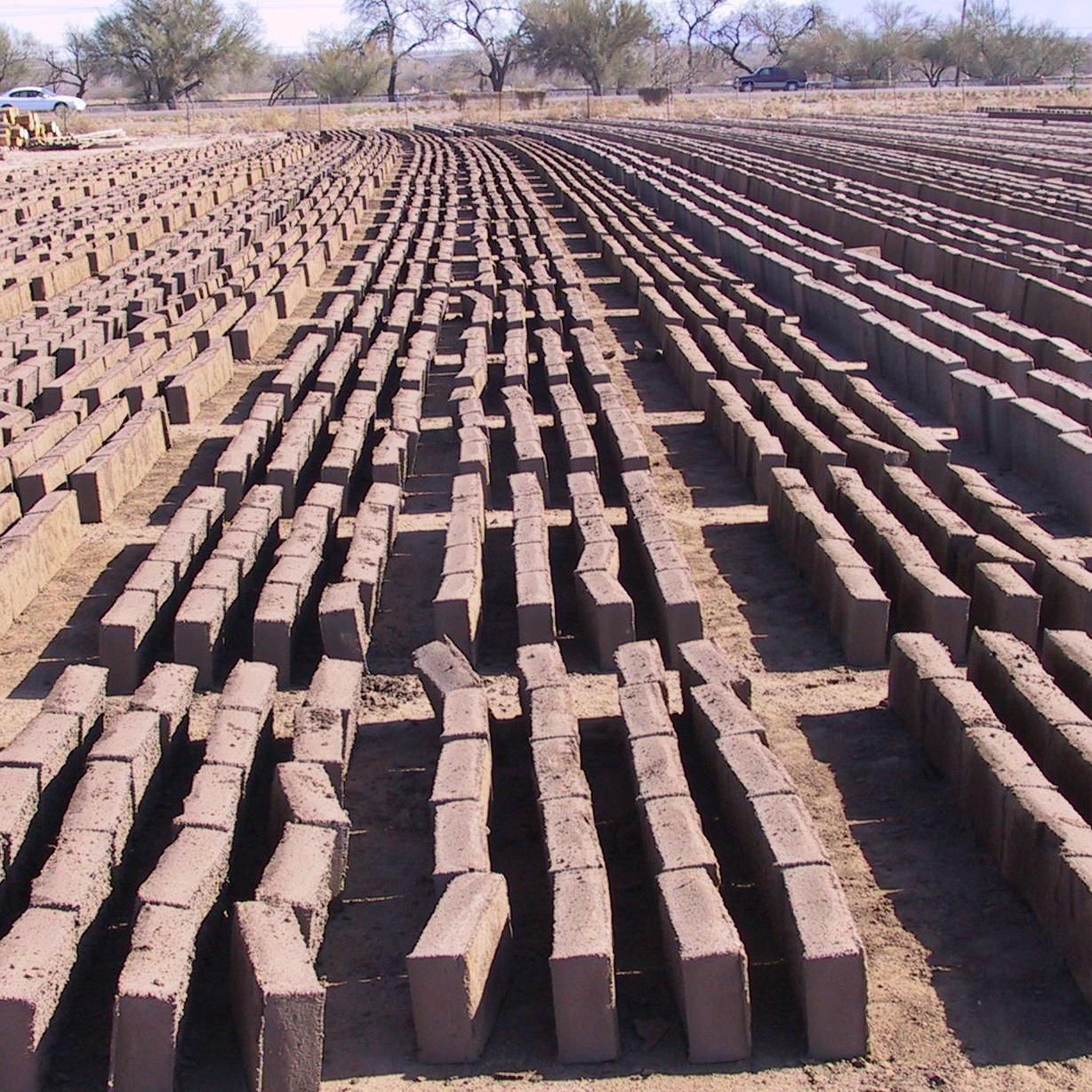 Rows of brown bricks in a field with trees in the background