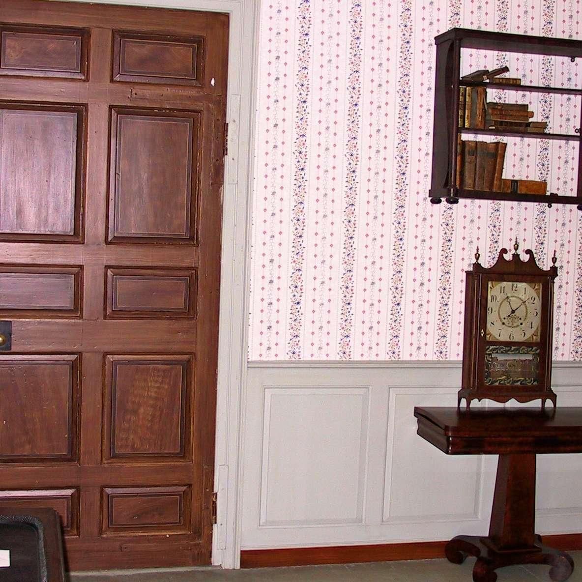 A room with a wooden door and a clock on a table