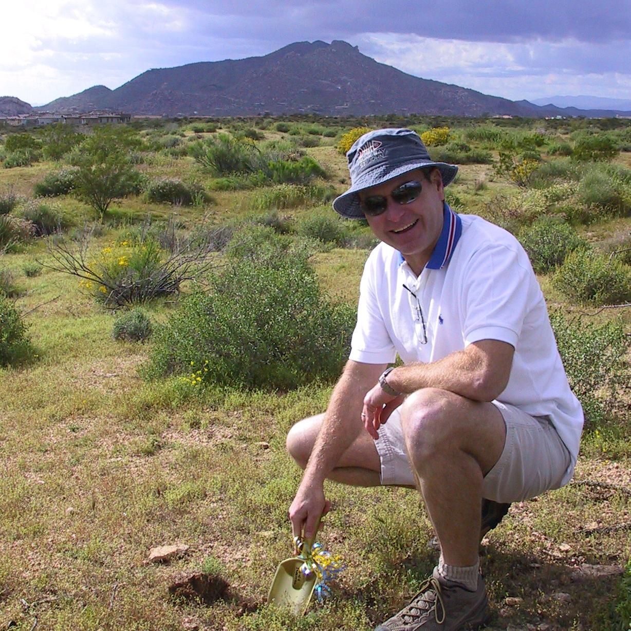A man wearing a hat and sunglasses is kneeling down in a field