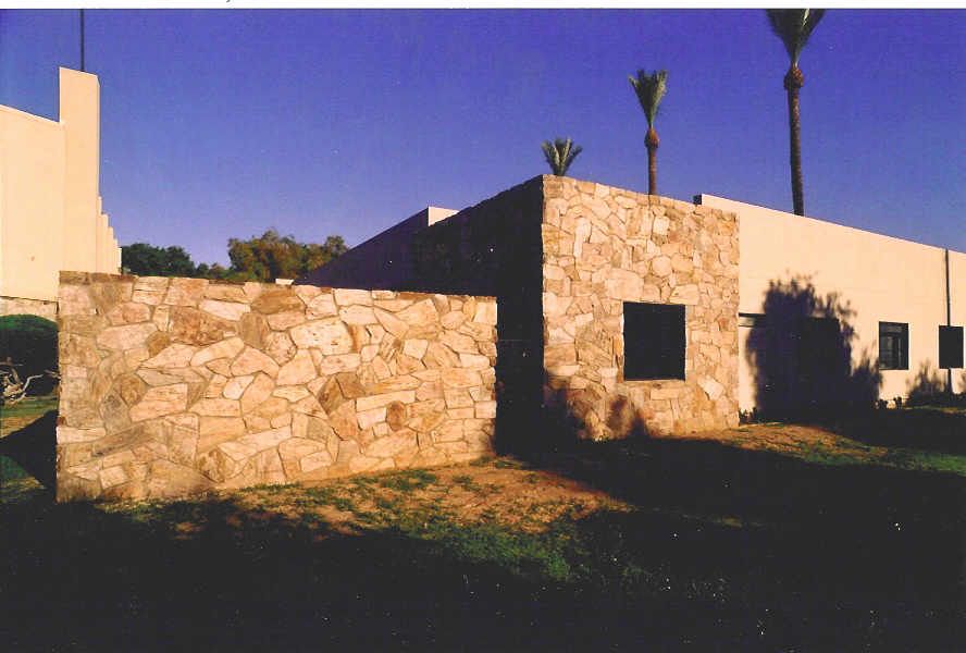 A stone wall surrounds a white building with palm trees in the background