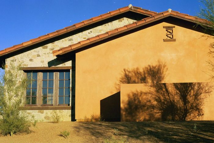 A house with a brick roof and a shadow of a bush on the side