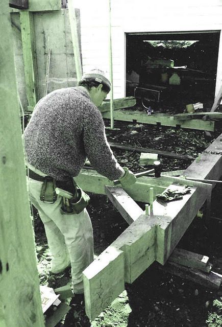 Man in work clothes assembling wooden beams outdoors.