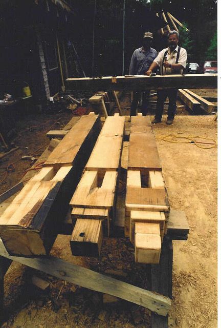 Wooden beams with carved notches, two men in background working on a wood structure.