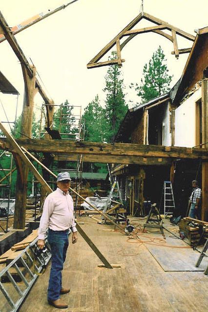 Construction site with a man, beam being lifted, wooden beams and building.
