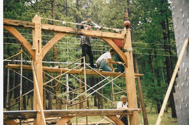 Construction workers on scaffolding building a wooden structure outdoors.