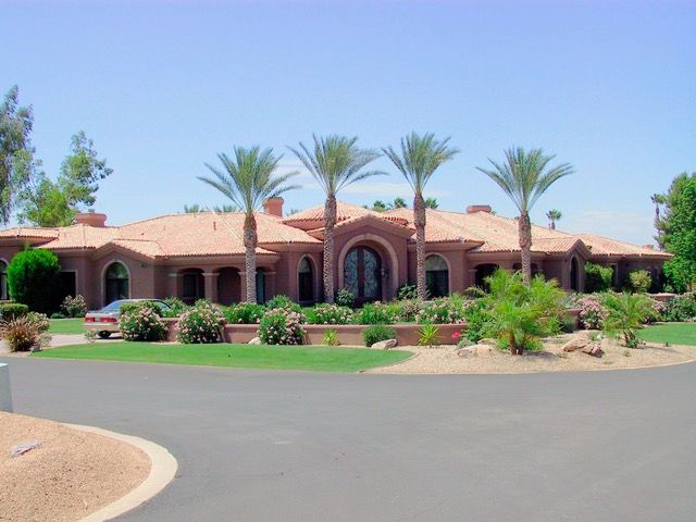 Large, single-story house with red tile roof, palm trees in front, and circular driveway.