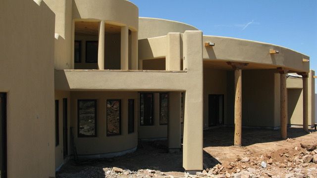 Beige stucco home with curved walls and wooden supports; sunny outdoor setting.
