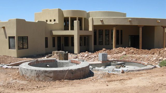 Southwest-style house with stucco exterior, under construction. Circular water feature in foreground; dirt lot.