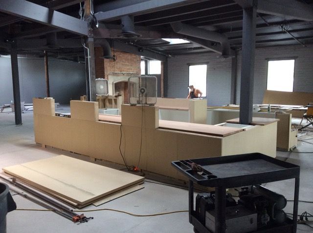 Large room under construction, featuring a partially built U-shaped structure, exposed beams, and a person in the background.