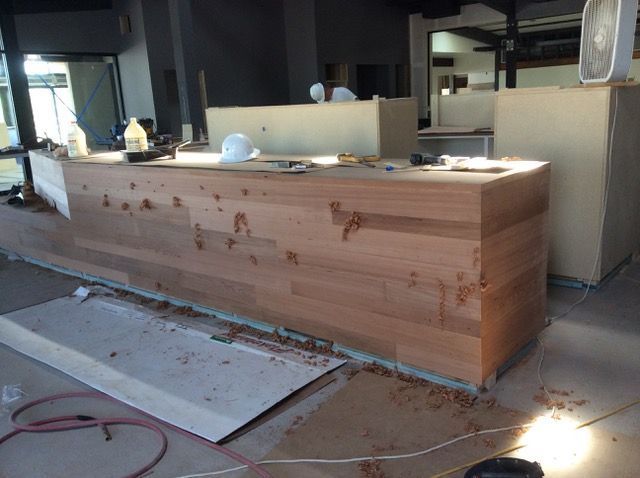 Wood counter under construction; two workers in background, tools and sawdust visible.