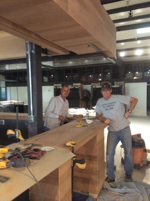 Two men building a bar. Light-colored wood, tools on the bar, inside a building.