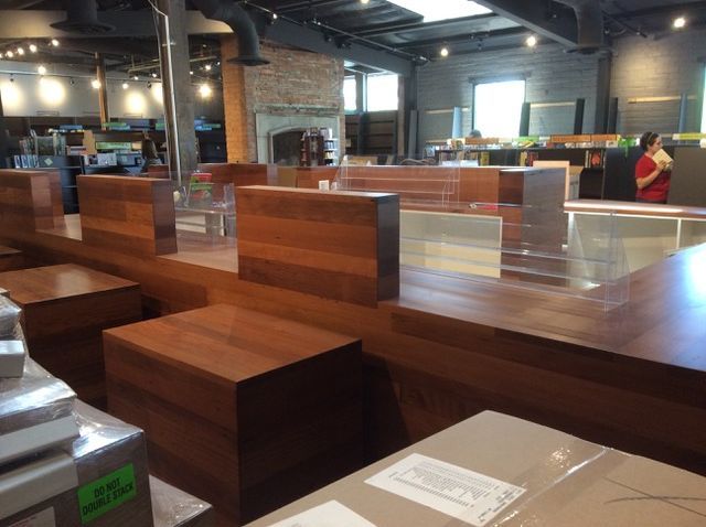 Wooden retail display in a store, with boxes in the foreground and a person in a red shirt in the background.