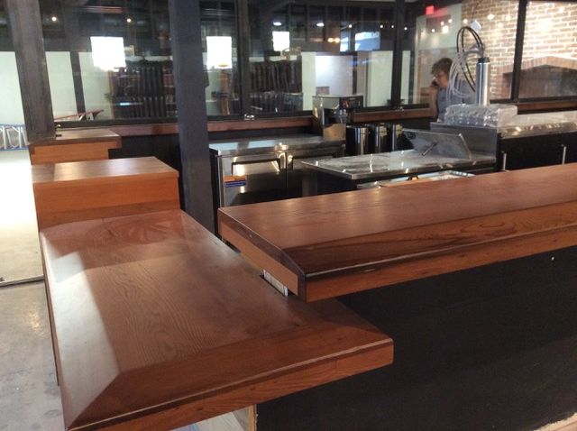 L-shaped wooden bar with stainless steel equipment in a restaurant setting.