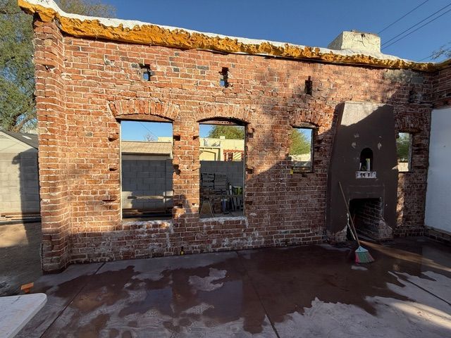 Ruined brick wall with window openings and a small hearth, sunlit with a wet floor in front.