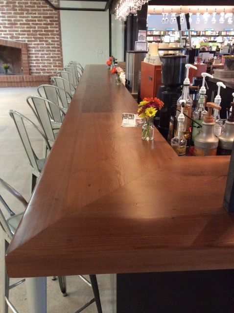 Long wooden bar with metal chairs; brick fireplace in background.