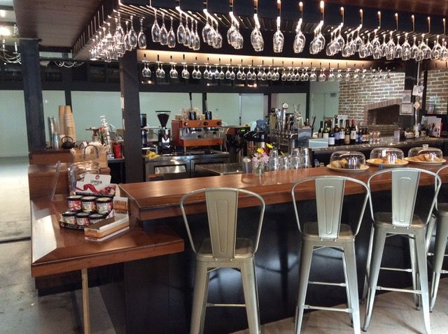 Bar counter with metal stools, glasses overhead. Bottles, coffee machine visible.