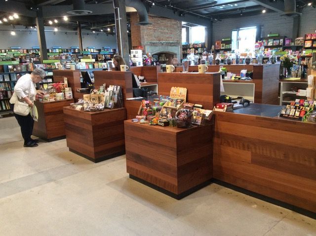 Woman browsing merchandise at the checkout counter of a bookstore with wooden fixtures and merchandise displays.