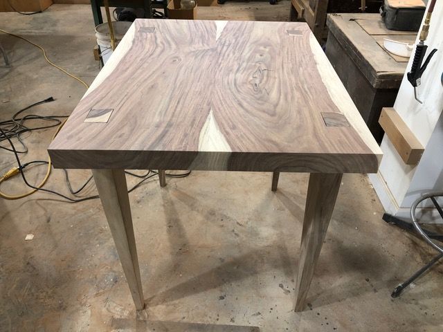 Wooden table with light-colored legs, dark-stained top with butterfly joints, set in a wood shop.