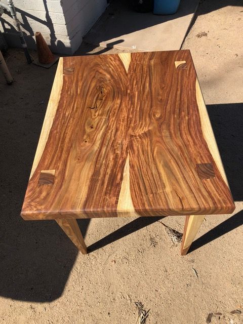 Wooden table with a dark, patterned top and light-colored legs and trim, outdoors.