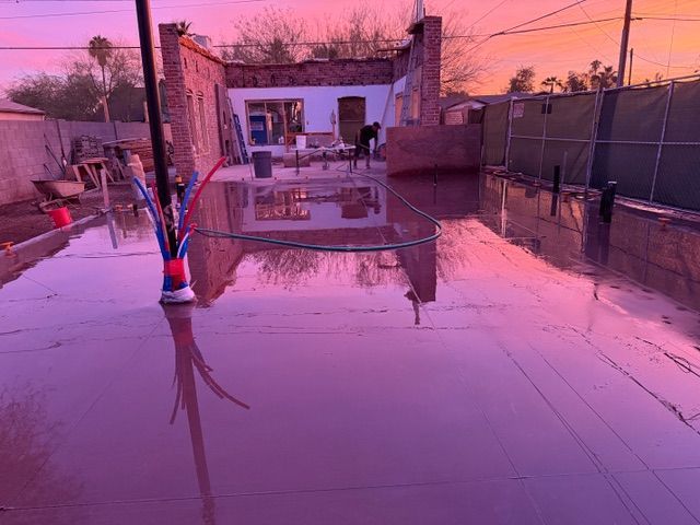Flooded backyard patio at sunset with pink reflections and a small white building in the background