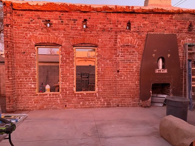 Red brick courtyard wall with two windows and a small arched doorway in warm evening light