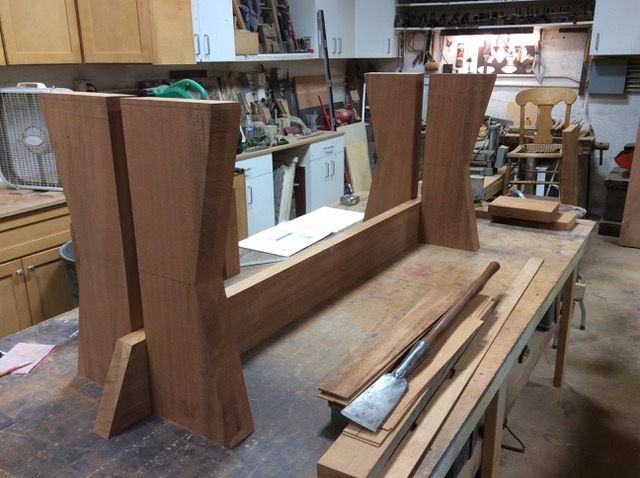 Wood table base under construction in a workshop. Brown wood, tools, and cluttered workbench.