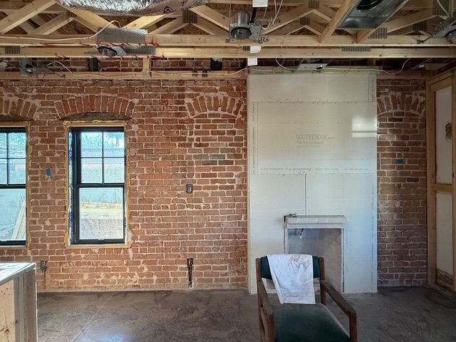 Brick loft interior with exposed beams, two windows, and a white fireplace wall.