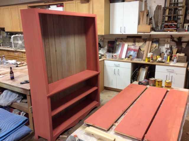 Red painted bookcase, disassembled shelves nearby, in a wood shop.