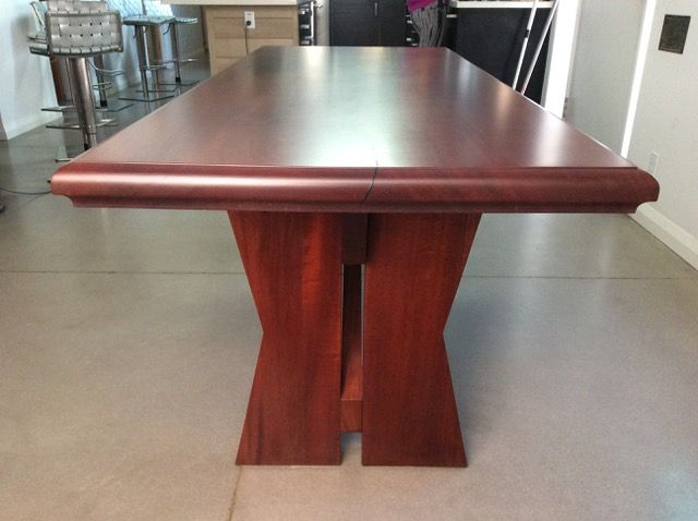 Wooden rectangular dining table with curved edges and hourglass-shaped legs.