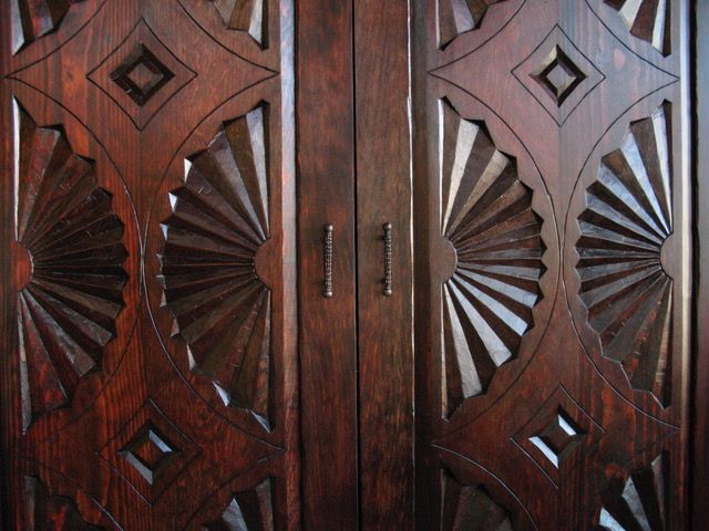 Wooden dining table with rounded edges and an X-shaped base in a well-lit room.