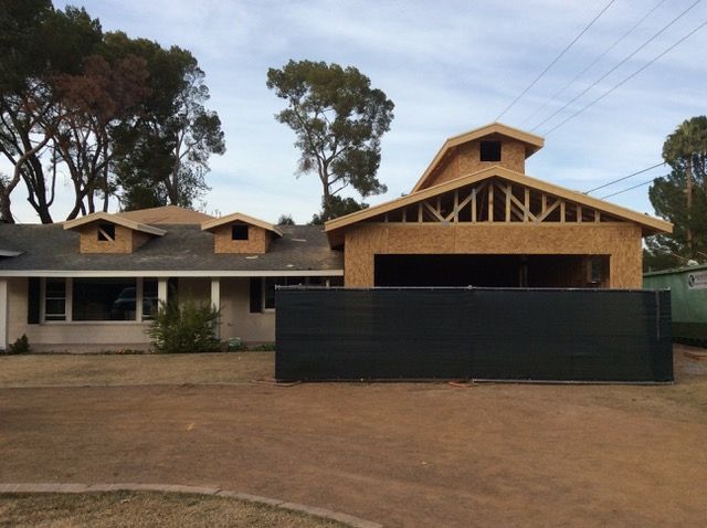 House under construction with exposed wooden frame, new garage addition, and dormers.