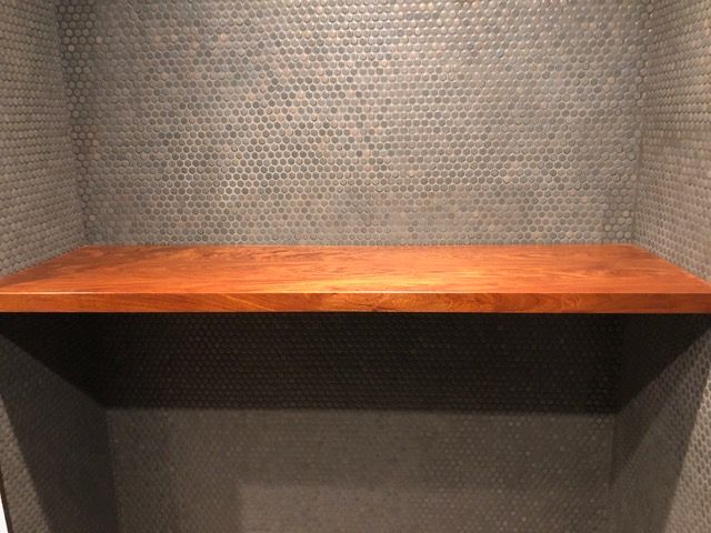 A wooden shelf is mounted within a nook with textured gray walls.