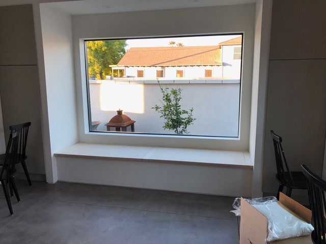Window seat with view of a white wall, building with a red tile roof, and a small tree.