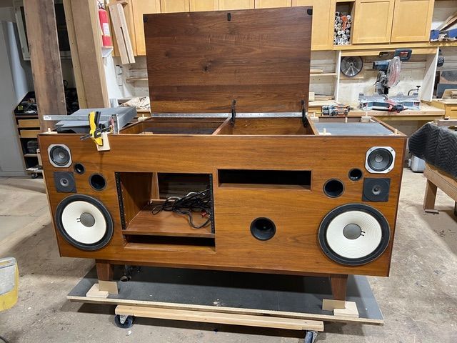 Wooden stereo cabinet with speakers, open top, in workshop setting.